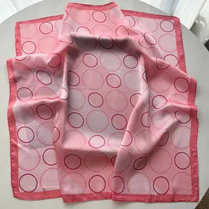 Detailed close-up of pink geometric silk scarf with circular patterns on a white table