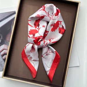 Elegant white silk scarf with red carnation floral print tied in a bow on a tray