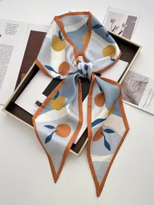 Detail of silk-satin skinny scarf with orange print tied on a dark display stand