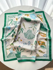 Close-up of floral and seashell print silk scarf with green border on a white table