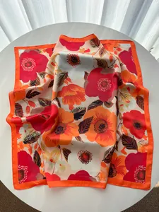 Detail van een zijden sjaal met oranje bloemenprint en hoogwaardige gezoomde rand