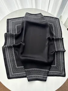 Close-up of black silk square scarf with white paisley and geometric patterns on a table