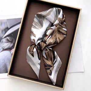 Detail of silk-like monstera print scarf folded in a premium brown gift box with magazine