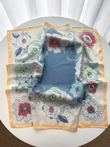 Carré de soie à imprimé floral avec centre bleu clair posé à plat sur une table blanche