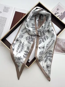 Close-up of silk scarf with black leaf print and brown borders on a golden tray