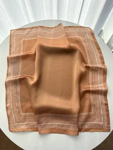 Detail of caramel silk satin square scarf with vintage paisley border on a table