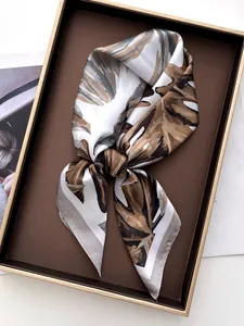 Detailed view of monstera leaf print satin scarf knotted inside a luxury gift box