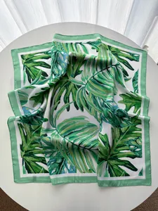 Detail of tropical monstera leaf print on silky scarf with green border and satin finish