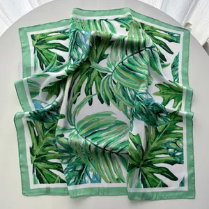 Detail of tropical monstera leaf print on a green and white silk square scarf
