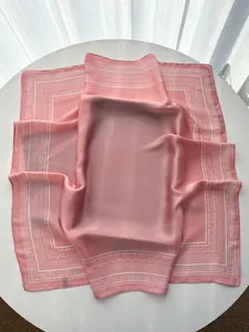 Detail view of pink faux silk square scarf with white paisley border and smooth texture
