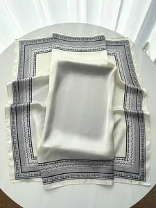Detail of silk satin scarf showing black paisley border and smooth cream fabric texture