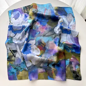 Artistic silk scarf detailing white lotus and blue dragonflies on a white surface