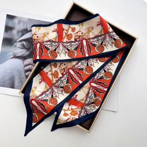 Detail of horse-print twilly silk scarf in orange and navy blue inside a gold gift box