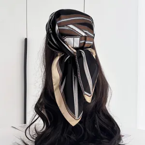 Detail of silk scarf tied as headwrap featuring classic black and gold chain patterns