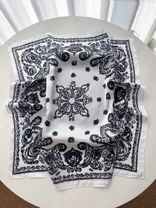 Close-up of white paisley silk scarf with black floral prints on a white table