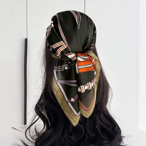 Detail of silk square scarf with luxury chain and belt print worn as a chic headwrap