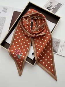 Detail eines Seidenschals in Ziegelrot mit Punkten, Blumenmuster und Geschenkbox