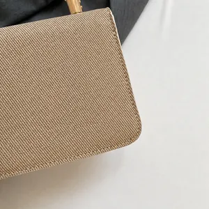 Detail shot of the woven linen texture and golden metal hardware on a beige handbag