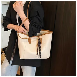 Vista detallada del bolso tote beige con contraste de cuero marrón y borla tejida chic
