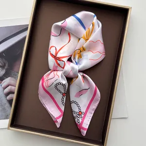 Nahaufnahme des rosa Seidenschals mit leuchtend rotem Schleifen- und Perlenkettenprint