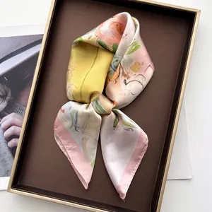 Détail d'un foulard en soie à peinture florale plié avec élégance dans un coffret cadeau brun