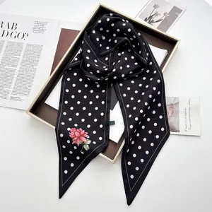 Detailansicht eines schwarzen Seidenschals mit Punkten und Blumen auf einem Tablett