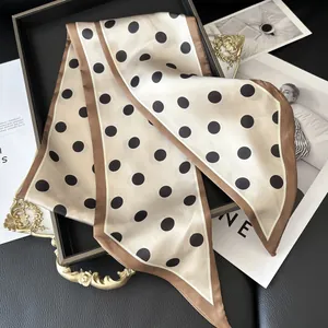 Detailed view of beige polka dot silk scarf with brown edges on a black leather tray