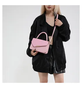 Pink linen textured handbag with gold metal bar worn by a model in a black outfit