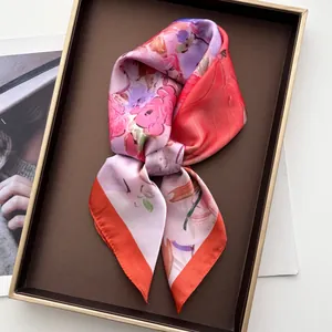 Gros plan d'un foulard en soie à fleurs avec bordure orange dans un plateau élégant