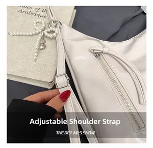 Detail of adjustable strap and pearl bow charm on white faux leather shoulder bag