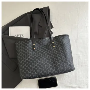 Close-up of black tote bag with M-pattern print, gold rivets, and a stylish art book background