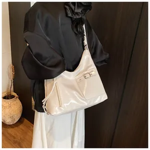 Side view of cream glossy patent leather tote bag with silver buckle on a female model