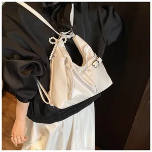 Detail of cream glossy hobo bag with pearl bow charm and adjustable silver hardware
