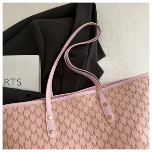 Close-up of pink tote bag with letter M print, fine leather texture and metal rivets