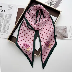 Nahaufnahme eines rosa Seidenschals mit roten Punkten und Blumen in einer Geschenkbox