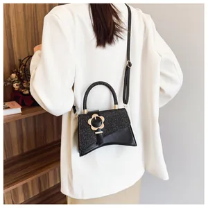 Détail du sac bandoulière à paillettes noires avec fermoir fleur dorée porté par un modèle