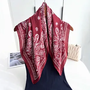 Deep red silk square scarf with white paisley pattern draped on a wooden hanger
