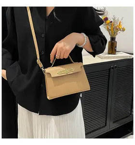 Detalle de bolso de cuero beige con cierre ovalado dorado y correa de hombro delgada