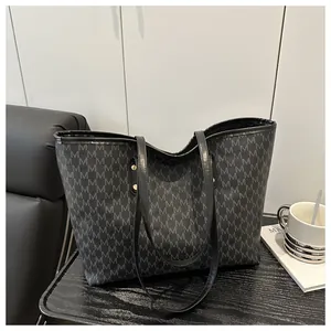 Detail of black leather tote bag with M-letter pattern and gold metal rivets on a desk