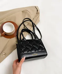 Detail van zwarte gewatteerde crossbodytas met gouden letters en stevig handvat bovenop