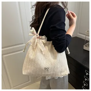 Détail du sac en paille avec logo nœud en métal et ruban en dentelle sur la bandoulière