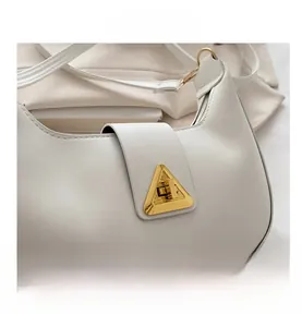 Close-up of white leather crescent bag featuring a prominent gold triangular turn-lock buckle