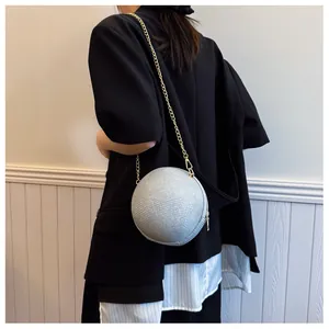 Silver spherical clutch bag with glittering texture and gold chain on model's shoulder