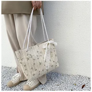 Detail der handgeflochtenen Strohtasche mit Blumenstickerei und weißer Spitzenschleife