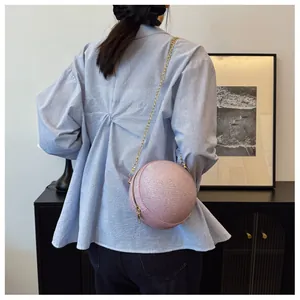 Detail view of a pink spherical crossbody bag with golden chain strap on a model