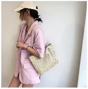 Detail einer beige Stroh-Tasche mit weißer Stickerei und einer Schleife aus Spitze