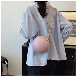 Close-up of pink sphere evening bag with woven texture and gold chain worn by a model