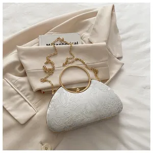 Detail of silver lace evening clutch featuring floral embroidery and gold metal ring handle