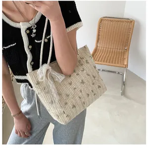 Details der beige geflochtenen Strohtasche mit grünen Herzen und weißer Spitzenschleife