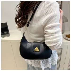 Detail of a black crescent underarm bag with a gold triangle buckle worn by a model